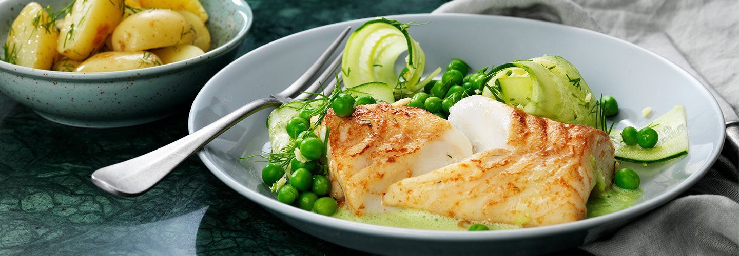 Pannestekt torsk i tallerken med grønne erter og agurk, poteter ved siden med urter. Flere oppskrifter med torsk på findus.no